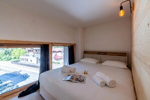 A hotel room with a bed, a window, a wall-mounted light, and a view of the outside.