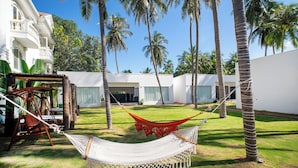 A hammock in a grassy area with palm trees and a white building in the background. - 3B MAISON Homestay & Villa (Mui Ne)