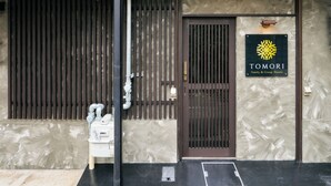 En bygningseingang med et metalhegn, et skilt med 'TOMORI Family & Group Hotels' og en vanddispenser udenfor.