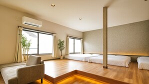 Et moderne hotelværelse med sofa, to senge, en potteplante og store vinduer.