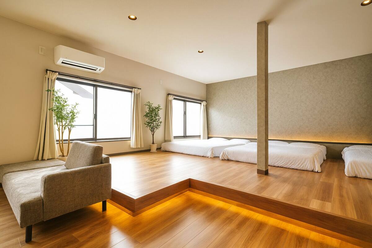 A modern hotel room with a sofa, two beds, a potted plant, and large windows.