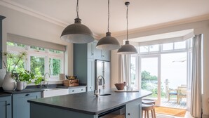 A modern kitchen with a central island, pendant lighting, and large windows offering a view of the outdoors. - The Wood -  a house that sleeps 15 guests  in 7 bedrooms (Salcombe)