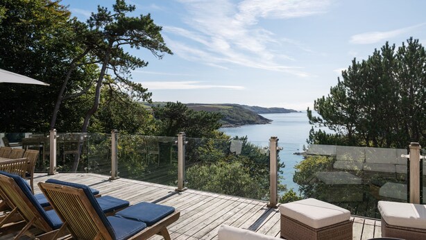 A wooden deck with lounge chairs and a glass balustrade overlooking a body of water and hills. - The Wood -  a house that sleeps 15 guests  in 7 bedrooms (Salcombe)