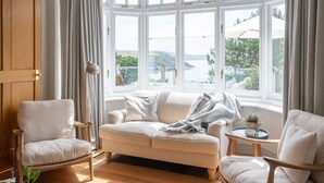A cozy room with a large bay window, a cushioned sofa, a wooden chair, and a small table with a tray. - The Wood -  a house that sleeps 15 guests  in 7 bedrooms (Salcombe)