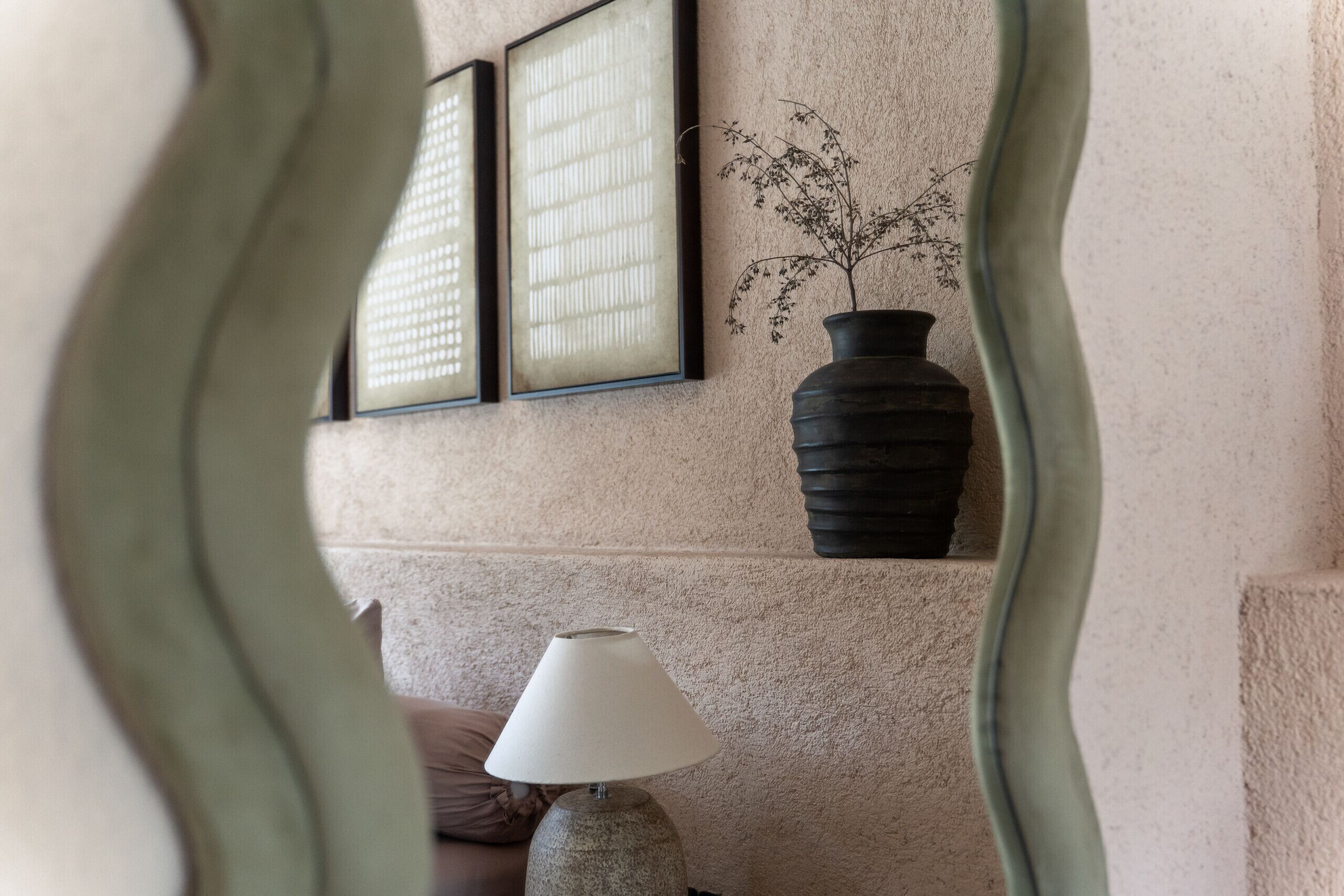 A room with a textured wall, a framed artwork, a vase with a plant, and a lamp on a table.