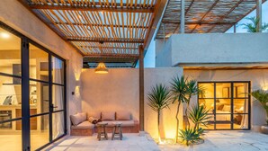 A modern outdoor living area with a wooden pergola, a sofa, two stools, and a dining table. - Sunset Rooftop | Private Pool | Quiet Canggu Villa (Canggu)