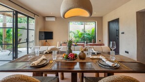 A dining area with a large table set for a meal, surrounded by wicker chairs, and a hanging light fixture above. - Sunset Rooftop | Private Pool | Quiet Canggu Villa (Canggu)