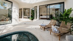 Un espacio de sala de estar moderno y abierto con piscina, mobiliario de mimbre y ventanas amplias.