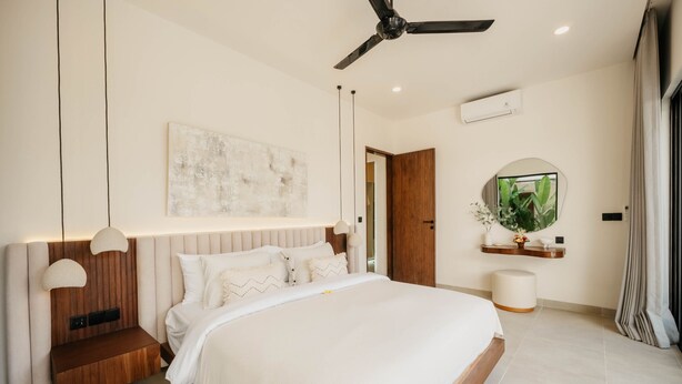 Un dormitorio moderno con una cama grande, un ventilador de techo, aire acondicionado instalado en la pared y una mesita de noche con lámpara.