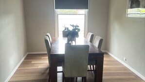 A dining area with a wooden table and chairs, a hanging light fixture, and a window with a view of greenery outside. - Awesome Central Horsham Home (Horsham)