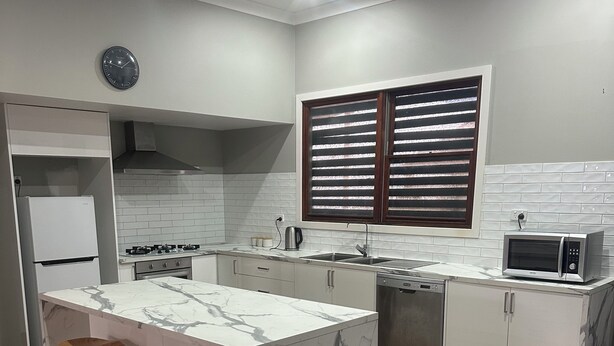 A modern kitchen with a marble island, wooden stools, a built-in oven, and a microwave. - Awesome Central Horsham Home (Horsham)