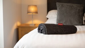 A neatly made bed with a rolled towel and a pillow, a bedside lamp, and a nightstand with a book. - Tigh Na Cille Studio (Taynuilt)