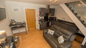 A compact living space with a kitchenette, a dining area, and a sofa with cushions. - Tigh Na Cille Studio (Taynuilt)