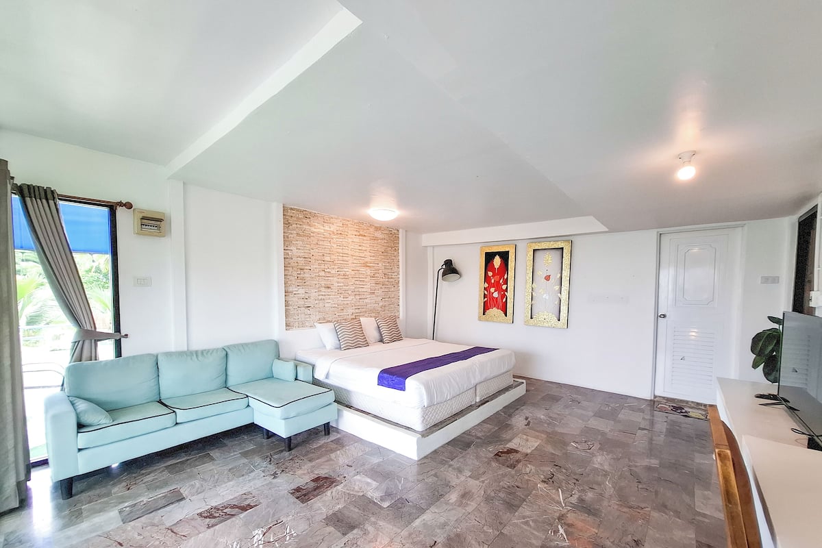 A bedroom with a bed, a light blue sofa, a brick accent wall, and two framed artworks.