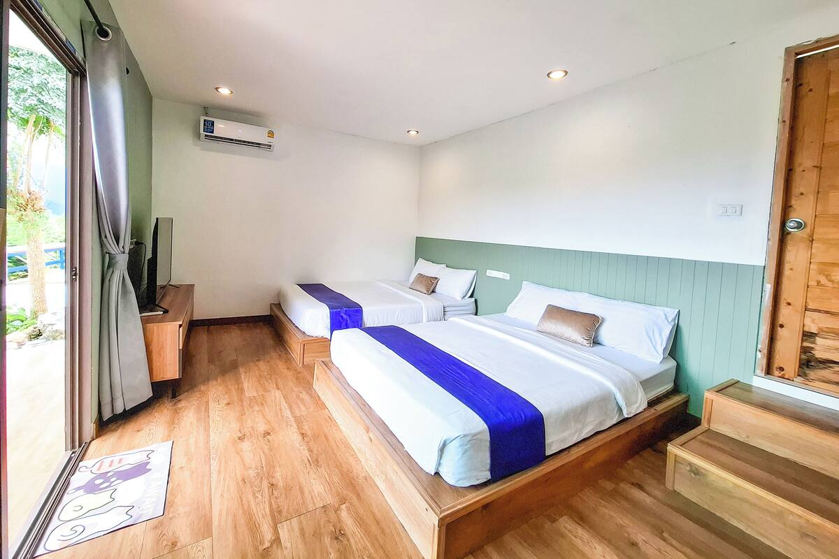 A room with two beds, wooden flooring, a television, and a door leading outside.