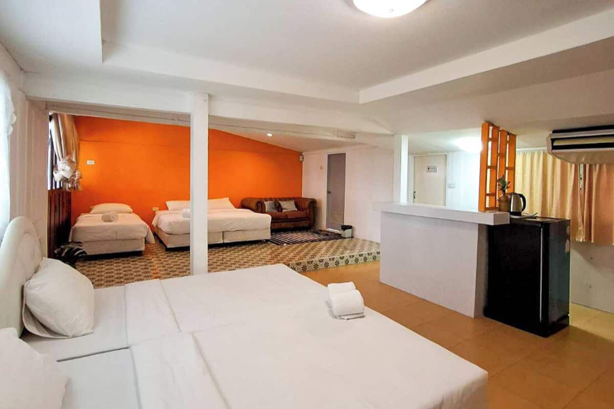 A hotel room with a large bed, two smaller beds, a sofa, a desk, and a mirror.