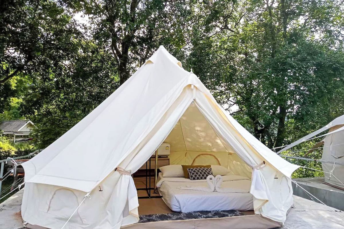 A tent with a bed inside, surrounded by trees.