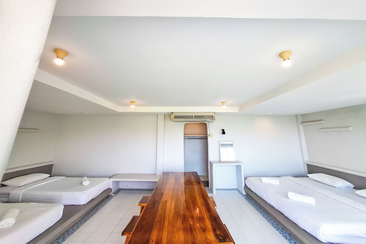 A hotel room with two single beds, a wooden table, a small white side table, and a ceiling fan.
