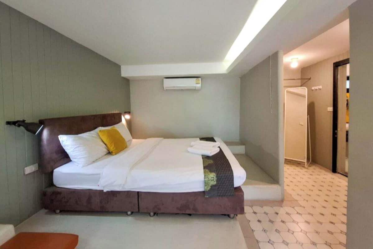 A bedroom with a bed, a bedside table, an air conditioning unit, and a bathroom door.