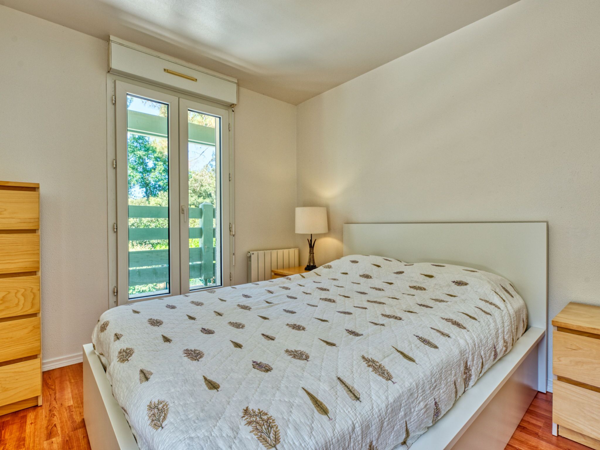 Une chambre à coucher comprenant un lit, une table de chevet, une lampe et une porte-fenêtre coulissante donnant sur un espace extérieur.