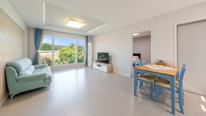 Un salon moderne comprenant un canapé, une table à manger avec des chaises, un téléviseur et une grande fenêtre avec des rideaux.