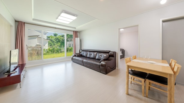 Un salon moderne avec un canapé en cuir, une table à manger avec des chaises et un téléviseur posé sur un meuble en bois.