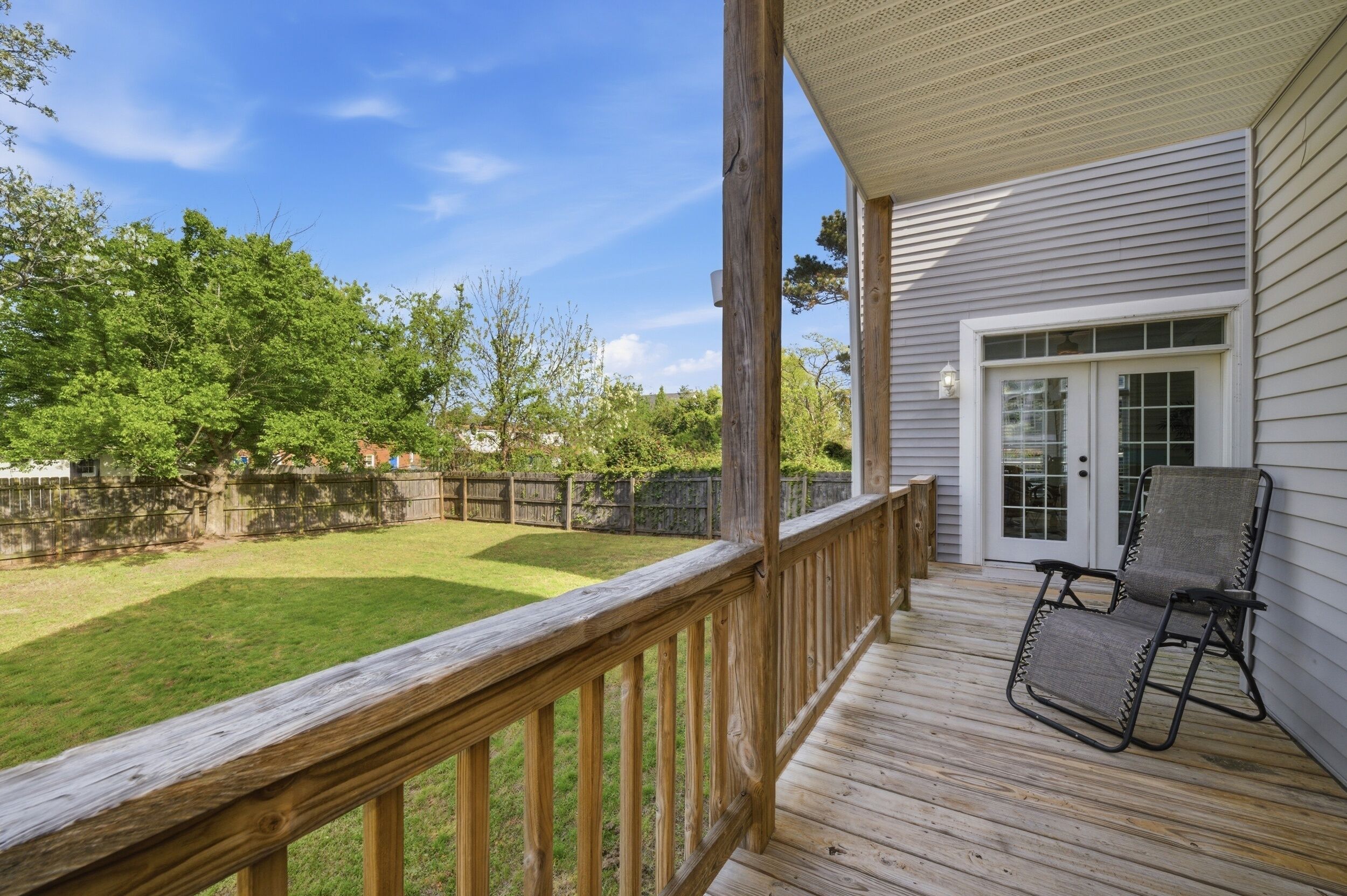 A wooden deck with a covered area, a door with glass panels, and a chair.