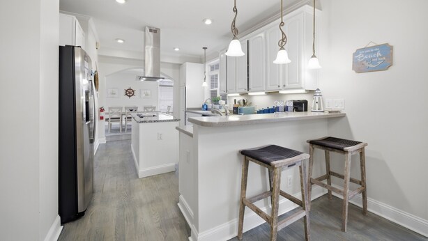A modern kitchen with white cabinets, a stainless steel refrigerator, pendant lighting, and a small island with stools. - 4 BR Beach Retreat - 2 Suites - Dogs Welcome (Norfolk)