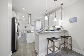A modern kitchen with white cabinets, a stainless steel refrigerator, pendant lighting, and a small island with stools. - 4 BR Beach Retreat - 2 Suites - Dogs Welcome (Norfolk)