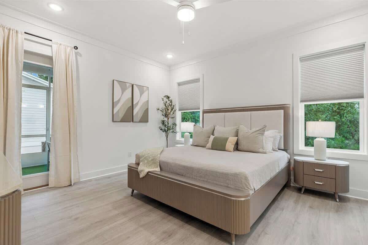 A bedroom with a large bed, a bedside table, a mirror, and a window with blinds.