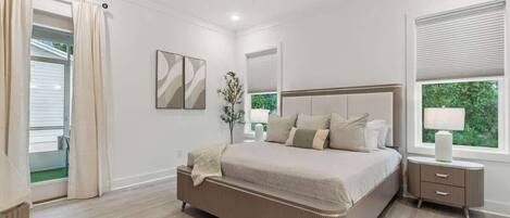 A bedroom with a large bed, a bedside table, a mirror, and a window with blinds.