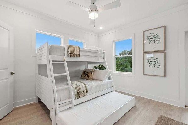 Habitación con literas, ventilador de techo, dos ventanas con vistas a la vegetación e impresiones botánicas enmarcadas en la pared.