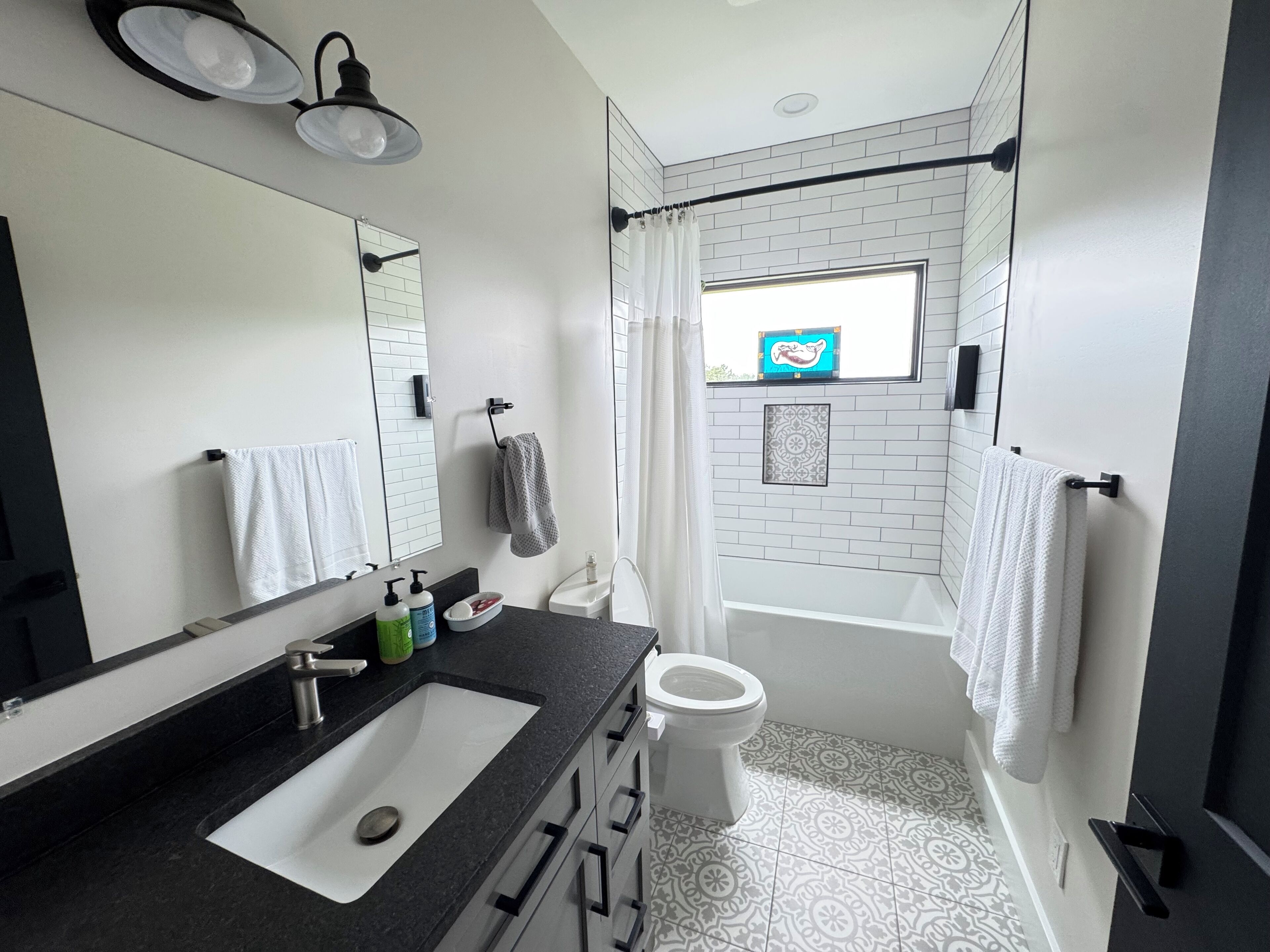 Un baño moderno con lavamanos de superficie negra, inodoro blanco y zona de ducha con ventana.
