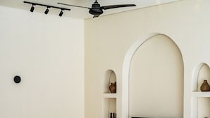 Una sala moderna con un televisor de pantalla plana grande montado en una pared blanca, un sofá color beige con cojines y un ventilador de techo.