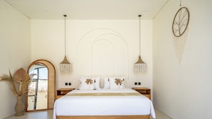 Un dormitorio moderno con una cama de madera, ropa de cama blanca, dos mesitas de noche, un espejo grande y un adorno en la pared.