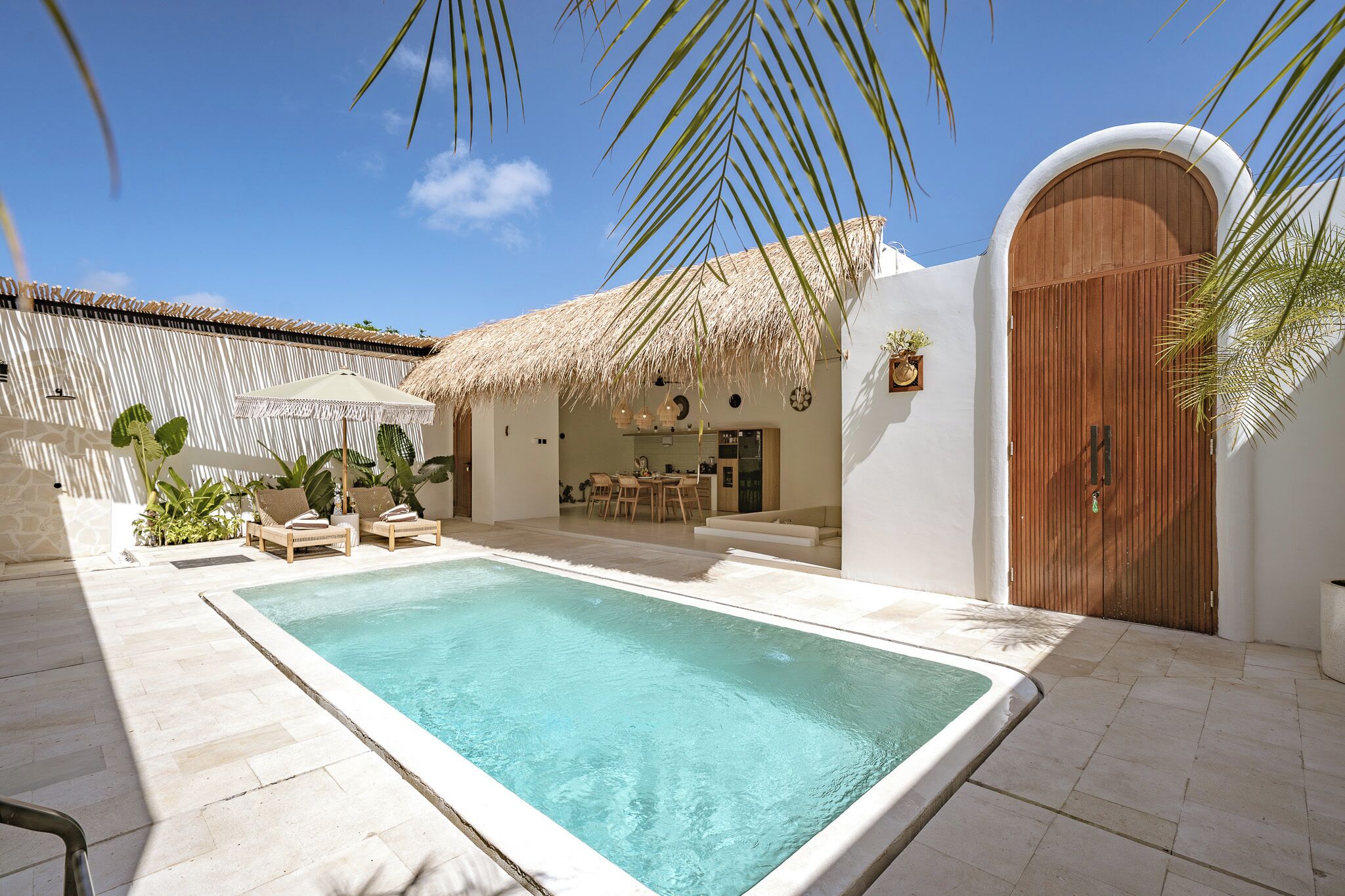 A pool area with lounge chairs, a thatched-roof structure, and a wooden door.