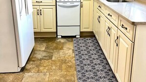 Una cocina compacta con armarios de color claro, un refrigerador blanco, un microondas, una estufa y un lavabo.