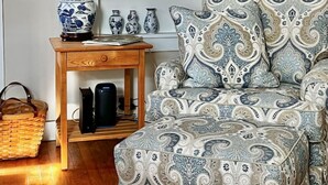 Una habitación con un sofá de tapicería azul y blanca, una mesita de madera con una lámpara azul y un estante en la pared que exhibe platos de cerámica azules y blancos.