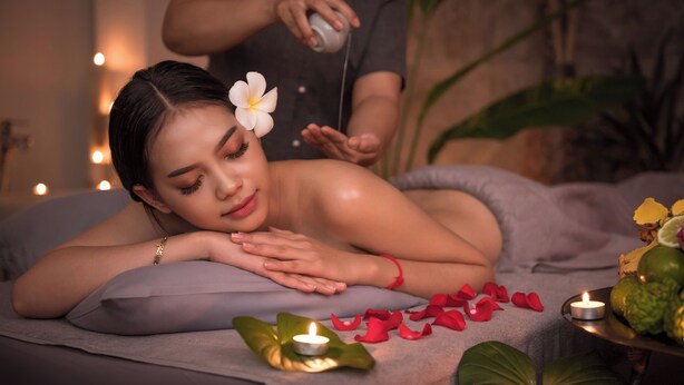 Wellnessbereich mit einer Person, die eine Massage erhält, einer Kerze und einer Fruchtschale.