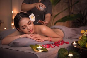 Een wellness omgeving met iemand die een massage ontvangt, een kaars en een schaal met fruit.