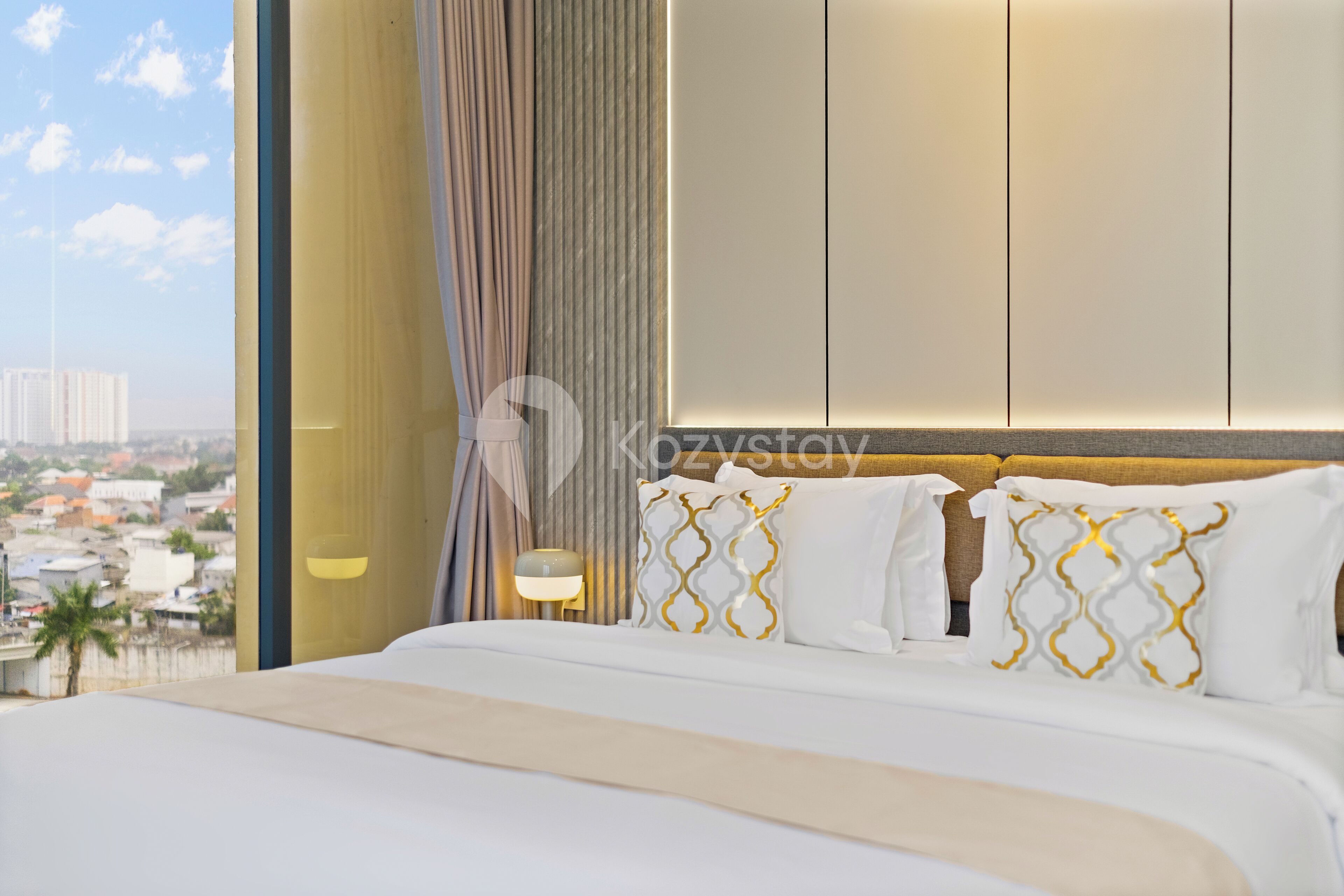 Een moderne hotelkamer met een groot bed, stadszicht en een groot raam met gordijnen.