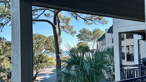 A view from a covered balcony overlooking a street with trees and a building.