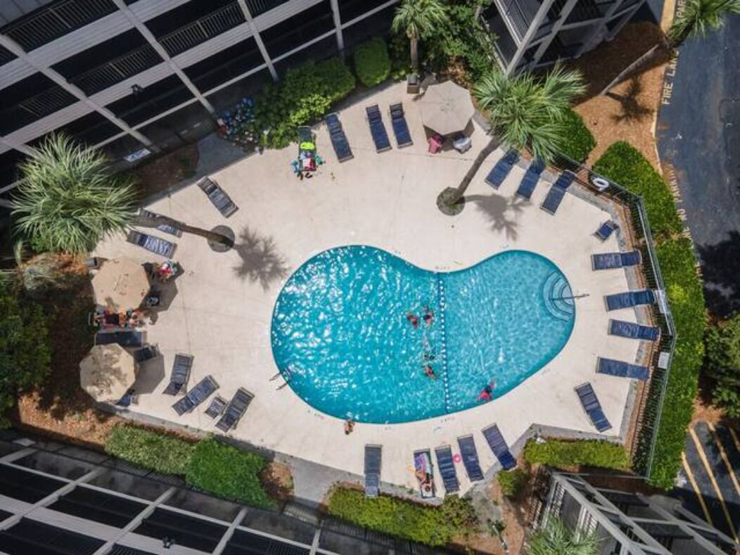 An aerial view of a swimming pool with lounge chairs and palm trees.