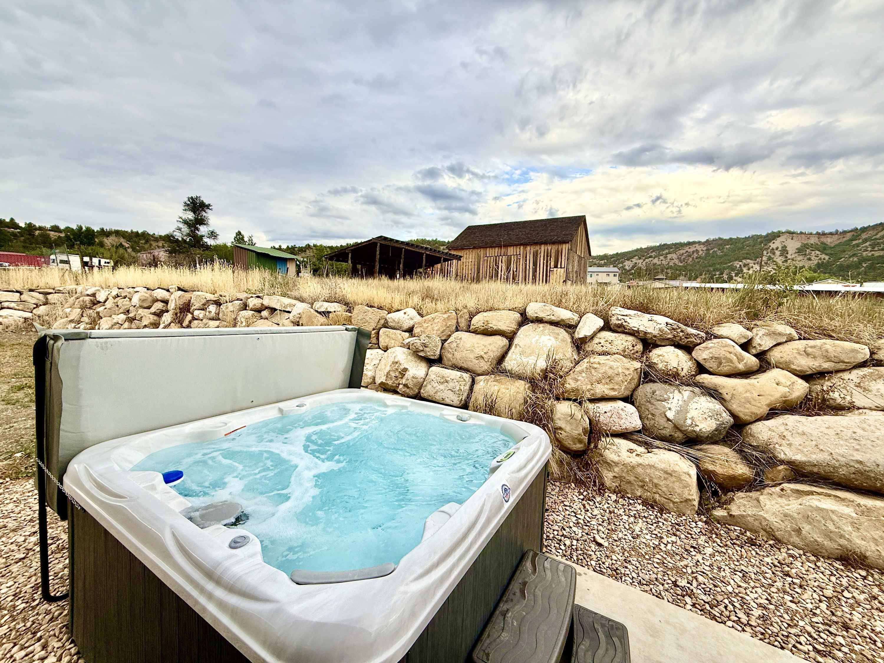 A hot tub in a rustic outdoor setting with a stone wall and a wooden structure in the background.