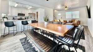 Una cocina moderna con armarios blancos, un comedor con mesa de madera y sillas negras, y un ventilador de techo.