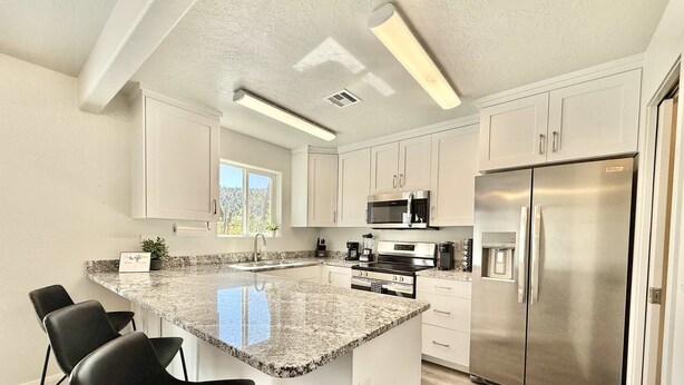 Una cocina moderna con gabinetes blancos, encimera de granito, electrodomésticos de acero inoxidable y una isla grande con taburetes de bar.
