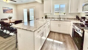 Una cocina moderna con armarios blancos, encimeras de granito, horno integrado y ventana con vistas.