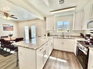 A modern kitchen with white cabinets, granite countertops, a built-in oven, and a window providing a view. - Glendale Retreat | Hot Tub Near Zion & Bryce (Glendale)