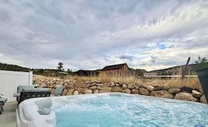 A hot tub with a stone wall and a rustic wooden building in the background. - Glendale Retreat | Hot Tub Near Zion & Bryce (Glendale)