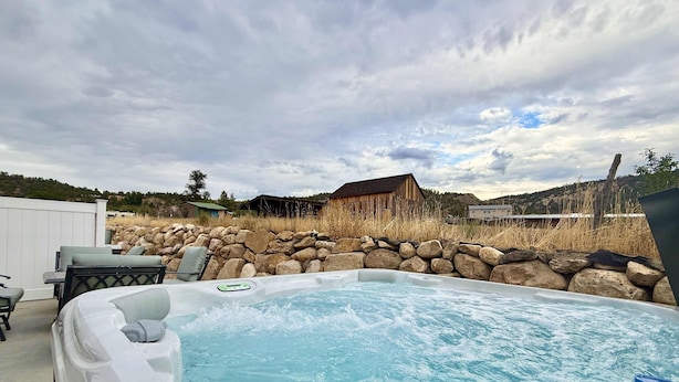 A hot tub with a stone wall and a rustic wooden building in the background.